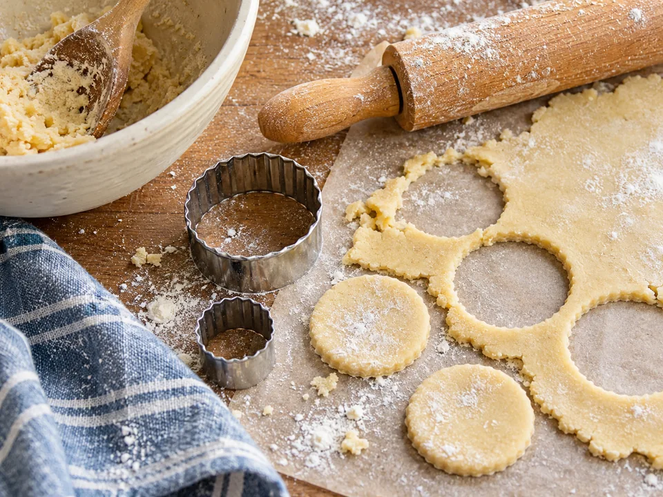 Close-up of biscuit dough, round cutters and a flour-dusted rolling pin.